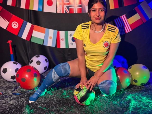 ZarayWhitMoreLove, voetbalmeisje, geel shirt, blauwe sokken, knielend, voetbal, kleurrijke vlaggen, zwarte achtergrond, groene en blauwe lichten, kleine borsten, gemiddeld achterwerk, donker haar, schattende glimlach..