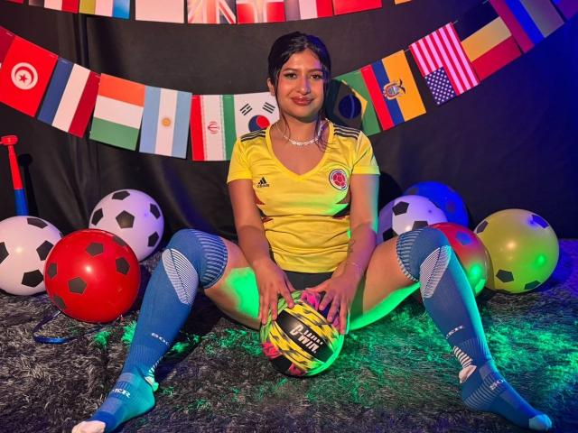 ZarayWhitMoreLove, Fußballspielerin, gelbes Trikot, blaue Socken, hält einen Ball, Beine gespreizt, bunte Flaggen, Fußballbälle, grüne und blaue Lichter, Teppich, dunkles Haar, kleine Brüste, süß, lächelnd..