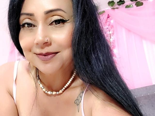 Zaria69 a de longs cheveux noirs, des yeux marron avec un trait d'eye-liner épais, un anneau au nez et un collier de perles. Elle sourit, avec du rouge à lèvres rose, et montre ses seins et un tatouage..