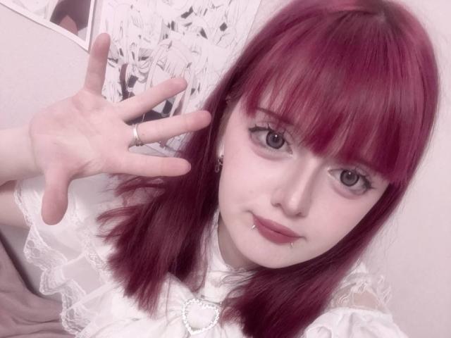 RobinKrapp with red hair, white lace top, septum piercing, and labret piercing, making a "rock on" hand gesture, showing a ring on her finger. Pale skin, blue eyes.