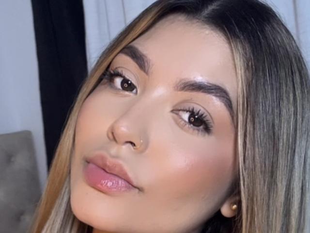 ArianneDelux ha un viso luminoso con pelle liscia, occhi marroni, lunghe ciglia e labbra rosa lucide. I suoi capelli biondi sono lisci e ha un piccolo piercing al naso..