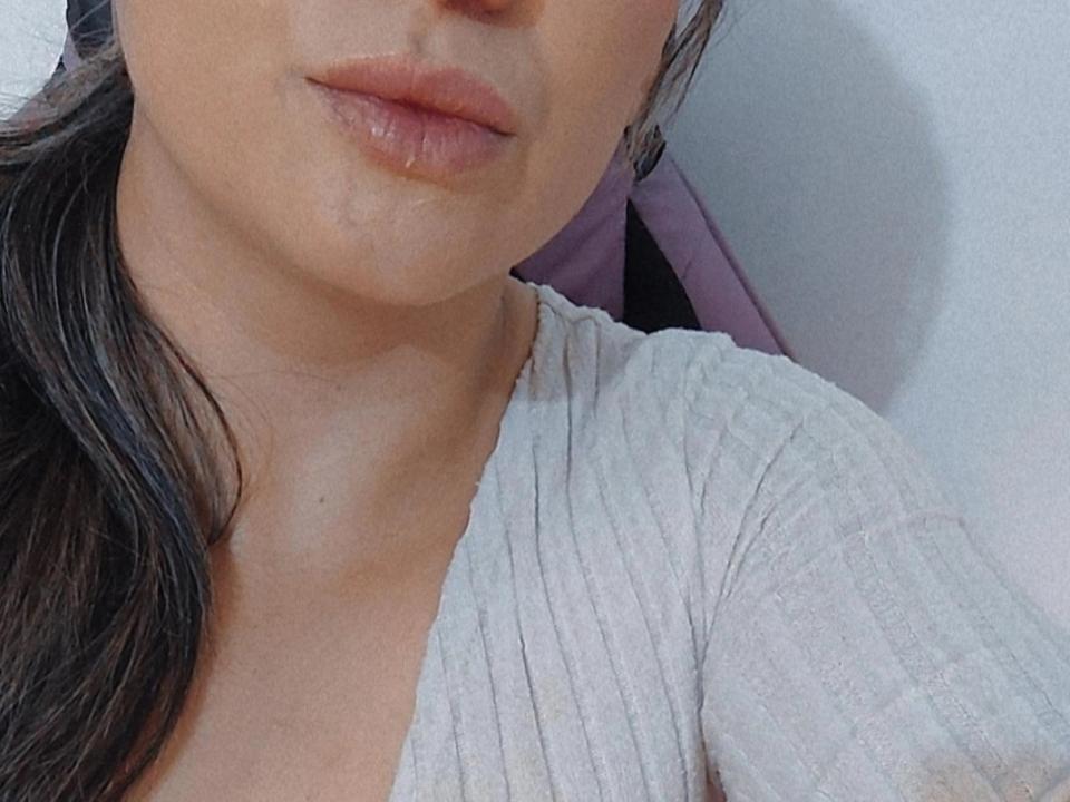 Soyrouse's face with slightly parted pinkish lips, wearing a ribbed white shirt, showing a small part of her brown hair. Her skin is light with a few subtle blemishes.