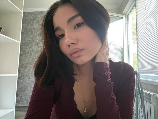 LaurineNghiem has dark brown hair, full eyebrows, and a serious expression. She's wearing a maroon rib-knit top, with her hand on her cheek and a necklace.