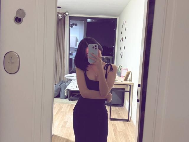 LaurineNghiem taking a mirror selfie, wearing a black strapless dress that hugs her curvy ass, holding a phone with a pink case, standing in a wooden-floored room.