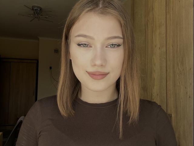 BobbyeWelson ha i capelli castano lisci, gli occhi verdi e indossa una camicia marrone con un rossetto rosso tenue. Le sue natiche non sono visibili. Sta sorridendo leggermente..