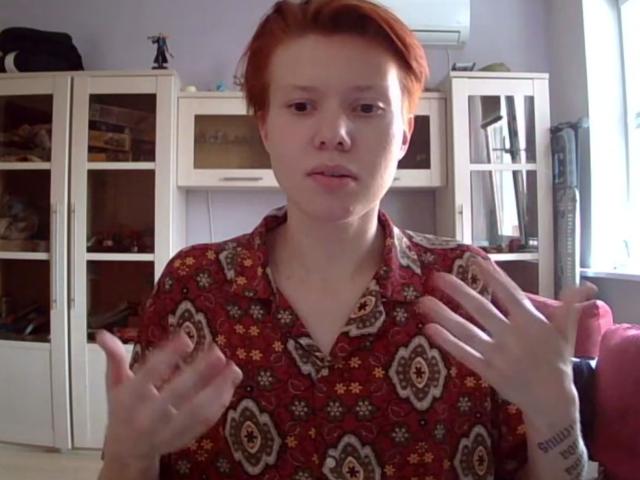 Carmelita Bemiller, con i capelli rossi, indossa una camicia rossa con fiori, ha le mani alzate e sembra leggermente confusa. Si vede un tatuaggio sull'avambraccio destro. Ha la pelle chiara, i capelli corti ed è in piedi in un ambiente interno..