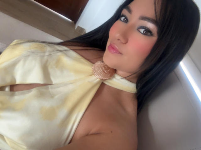 VanesaCandy with long black hair, pink lipstick, and pink blush, wearing a yellow tie-front top, showing her bare shoulders and a hint of her tits.