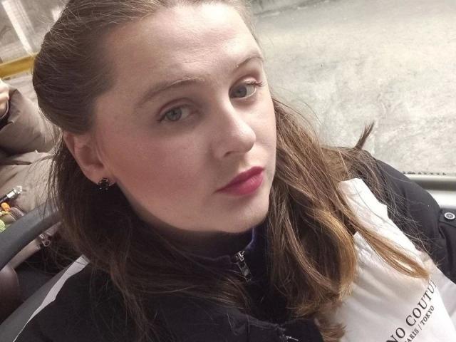 BettyBloom-hot ha la pelle chiara, i capelli castani, gli occhi azzurri, il rossetto rosso e indossa una giacca nera e bianca, con piccoli orecchini neri, e guarda leggermente di lato..