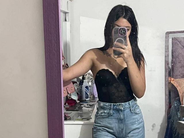 ScarlettPreatty with black lace bustier, showing her tits, and blue high-waisted jeans, taking a mirror selfie with her phone, in a bedroom. Her black hair is down.
