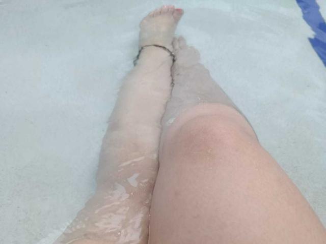 As pernas de IvonnaLune estão em uma piscina, com a água chegando até a metade da coxa, e ela usa uma pulseira preta no tornozelo direito. Seus joelhos estão ligeiramente afastados..