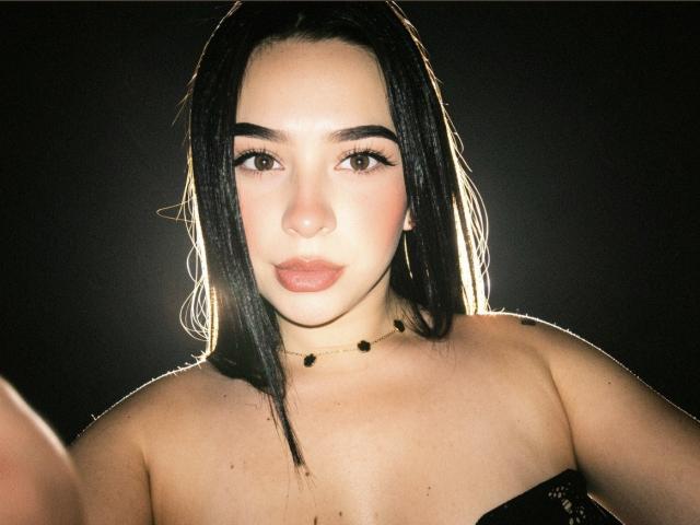 MiaAylen has dark, straight hair, light skin, and brown eyes. She's wearing a black strapless top with a bead necklace, and her full, pouty lips are slightly parted.