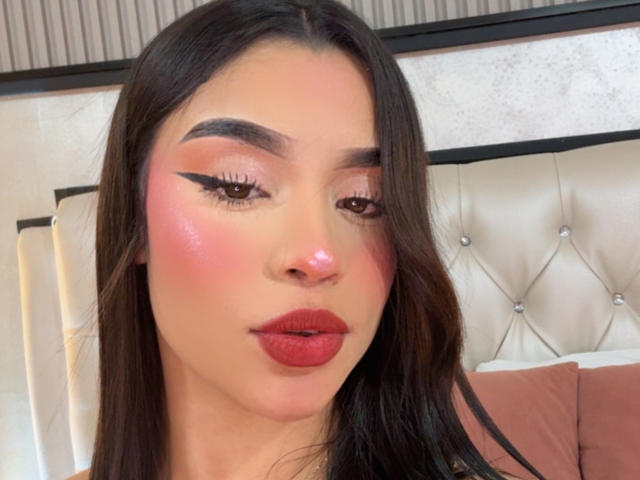 LunaVali a des joues roses brillantes, un trait d'eye-liner noir audacieux, de longs cheveux bruns, du rouge à lèvres rouge et une bouche légèrement entrouverte, avec un brillant rose. Ses sourcils sont épais et foncés..