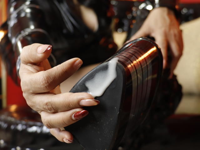 AliceCarusso's hands with red nail polish are wiping white fluid from the heel of a black, shiny, metallic boot. Her fingers are gripping the boot firmly.