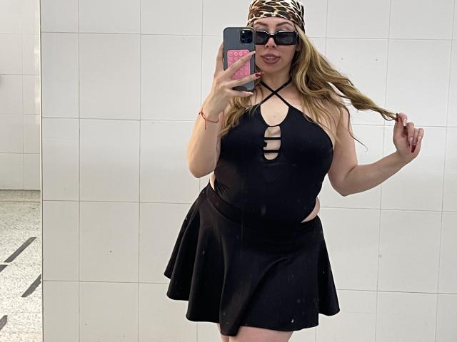 JennyLawry with long blonde hair, wearing a leopard print headband, black halter top with cut-out, and black skirt, holding phone in mirror selfie, flaunting her big ass.