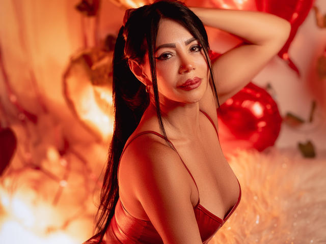 HelenHard with long black hair, red lingerie, and medium tits, looking at the camera with a seductive smile, hand in hair, warm red-orange lighting, soft fluffy background.