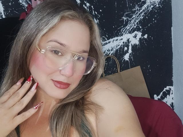 AlexaHotSeins with glasses, red lipstick, and red nail polish, showing her shoulder and hand, has blonde hair, and a cute face, with her tits slightly visible.