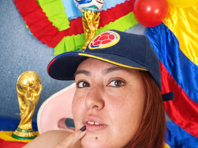 TerraMegaBoobs with freckled face, brown eyes, and red hair, wearing a blue cap with a red logo, touching her lips with a finger, and a golden trophy nearby.