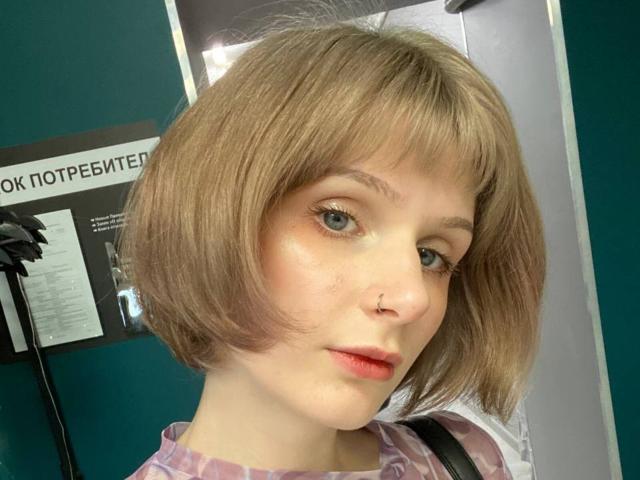JaimieLiley heeft een schattig kort kapsel met lichtbruin haar, blauwe ogen, een kleine neusring en roze lippenstift. Ze draagt een roze top met een patroon en kijkt iets opzij..