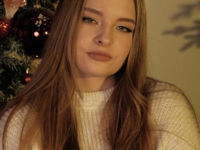 Malinda Bordwine a de longs cheveux bruns, une peau claire et porte un pull blanc en tricot. Ses yeux verts sont à moitié ouverts, et elle affiche un léger sourire satisfait. Ses seins sont partiellement visibles..