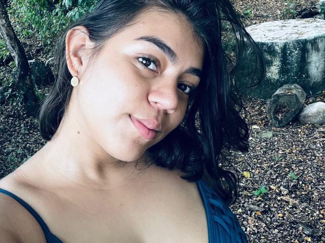 NaturalMia ha la pelle marrone media, i capelli neri e ondulati e piccoli orecchini. Ha la lingua rosa fuori, mostrando il naso e la sua canotta nera a spalline. Il suo seno non è visibile..