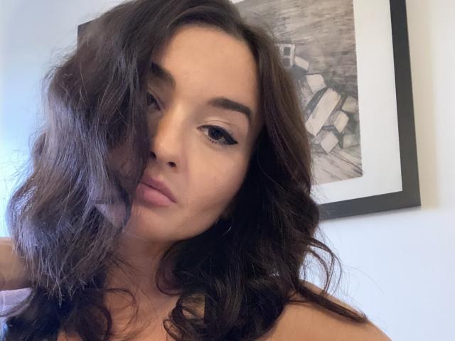 Dionisia, avec ses cheveux bruns foncés ondulés, son eye-liner noir intense et ses lèvres roses pulpeuses, regarde légèrement sur le côté, révélant son visage doux et bronzé ainsi que son maquillage discret..