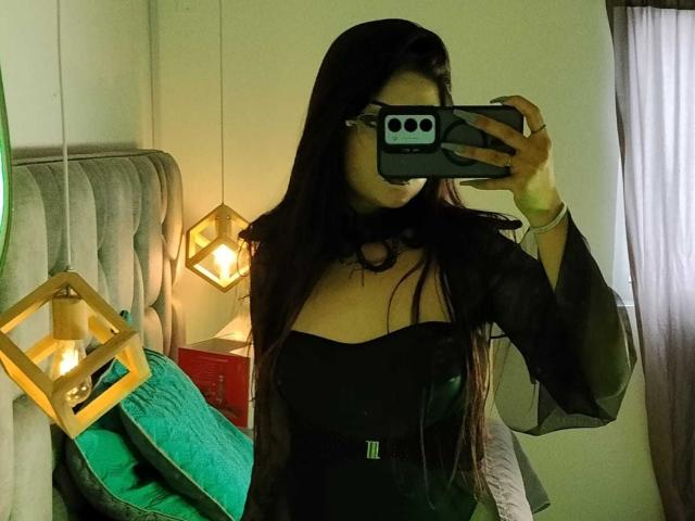 Helena Morningstar, con lunghi capelli scuri, un abito nero trasparente e una collana nera, tiene un telefono davanti al viso, mostrando il suo seno in un selfie allo specchio..
