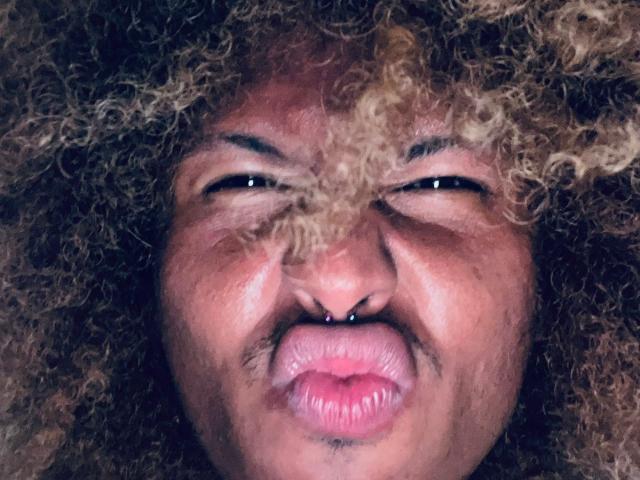 Il viso di AshleySofiaThenison, con i capelli ricci biondi e castani, un anello al naso e labbra rosa arricciate, gli occhi socchiusi, che appare leggermente infastidita o sorpresa..