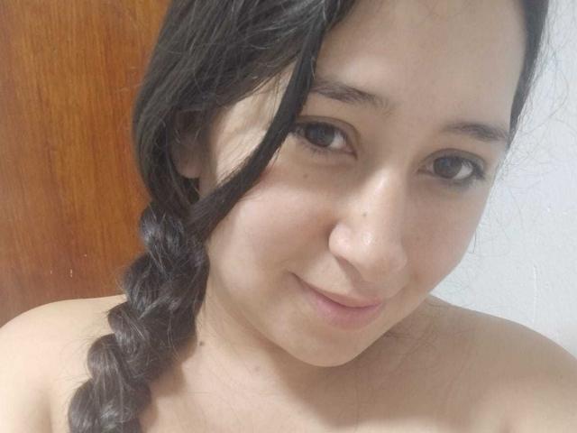 MelodyRosses has dark brown hair in a braid, light skin, and small tits, with a cute smile, and a small beauty mark on her right cheek, in a selfie.