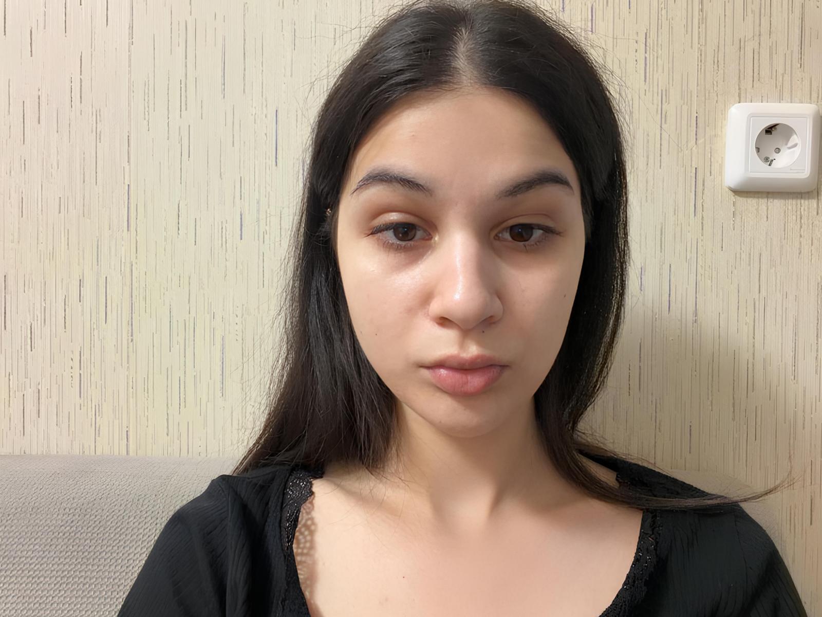 JameyDelira tem cabelos pretos longos, olhos castanhos e uma expressão neutra. Ela está vestindo uma blusa preta com detalhes em renda, e seu rosto está centralizado na foto..