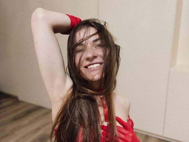 LumiEmma with long brown hair, red lingerie, smiling, arm raised, messy face, looking cute, wooden floor, red glove, standing, smiling, showing teeth, sexy, attractive.