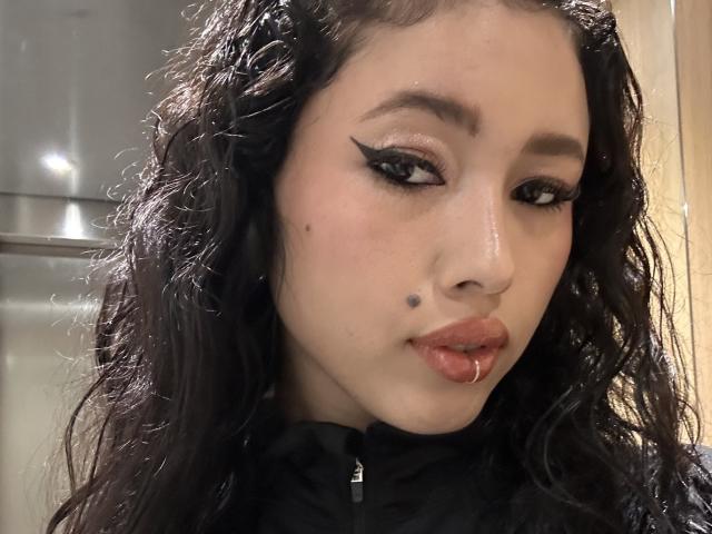 Nashiro Sakurai heeft krullend zwart haar, dikke zwarte eyeliner, een kleine zwarte moedervlek op haar linkerwang, en haar lippen zijn lichtjes open met een kleine rode stip..