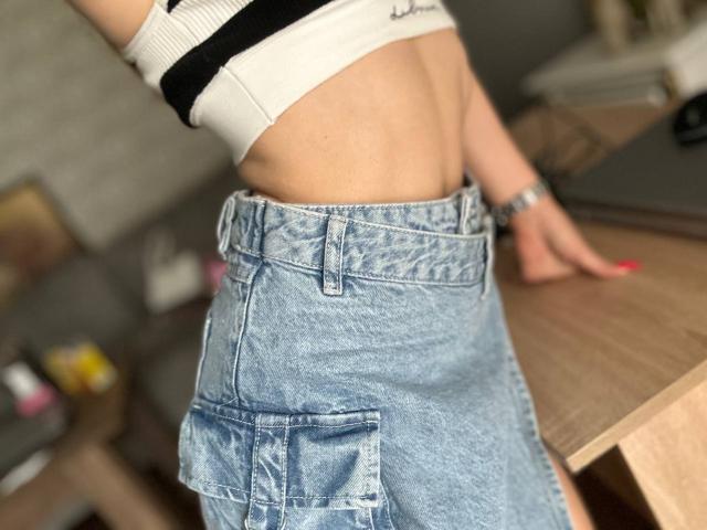 FortyLeride's bare midriff shows a toned stomach with a white ribbed crop top, wearing a blue denim skirt with pockets, and a silver watch on her right wrist.