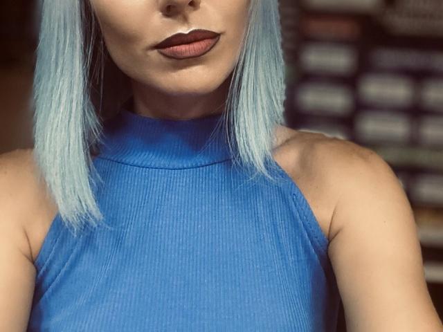 FortyLeride with blue ribbed sleeveless top, pale skin, blue hair, and dark lipstick, showing her upper body and tits, focused on her face and chest.
