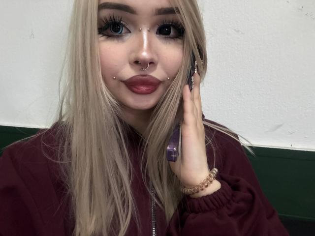 SerinaSindlinger has long blonde hair, blue eyes, and a nose ring. She's wearing a maroon hoodie, holding a phone, with a bracelet on her right hand.