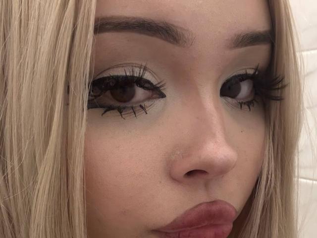 SerinaSindlinger's face with blonde hair, brown eyes, thick black eyelashes, and pink pouty lips. Her skin is light and her eyebrows are neatly shaped.