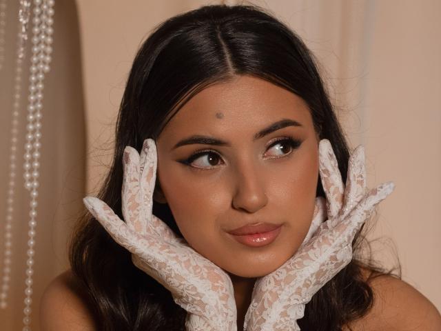 JasmineDay has dark brown hair, brown eyes, and a small beauty mark on her forehead. She's wearing white lace gloves, with her hands gently framing her face.