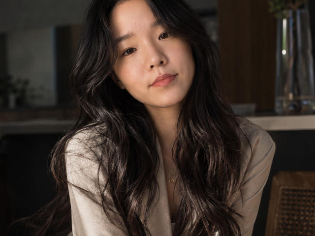 SamanthaTango has long, wavy black hair, light skin, and is wearing a beige shirt. She's looking at the camera with a subtle, relaxed smile. Her tits are small.