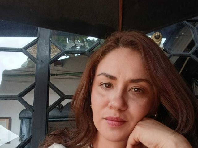 TheresaLarson a les cheveux bruns, un visage boudeur, et sa main repose sur sa joue. Elle regarde l'appareil photo avec une expression légèrement agacée. Elle porte une chemise blanche..