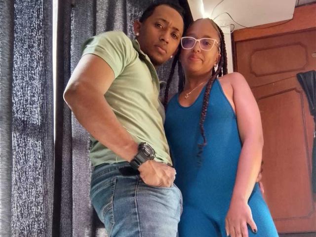 LilithAndAsmodeo in a green shirt and blue jeans with a watch, standing next to LilithAndAsmodeo in a blue dress and glasses, both with serious expressions.