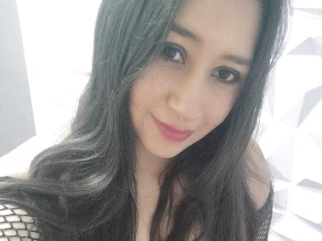 MelodyRosses has long black hair, light skin, and pink lipstick. She's smiling with dark eyeliner, wearing black fishnet sleeves, and has a cute, sexy face.
