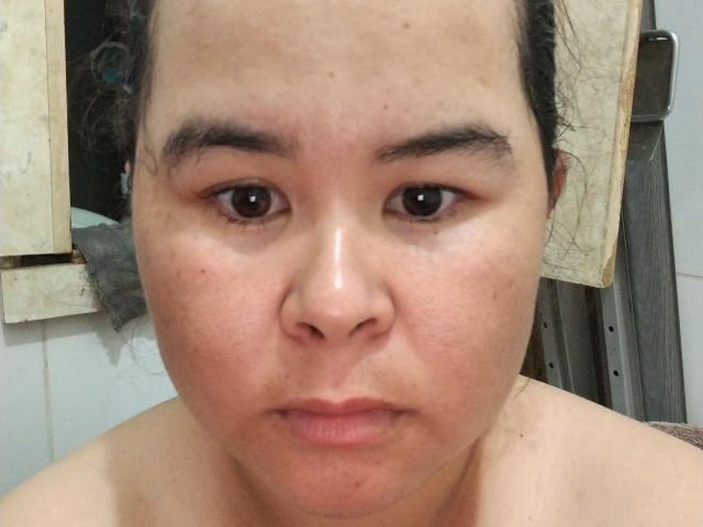 Le visage de MissJogurt, avec son nez rond, ses lèvres légèrement entrouvertes et ses sourcils foncés, et ses yeux marrons fixant directement l'appareil photo, présente une peau brillante et huileuse..