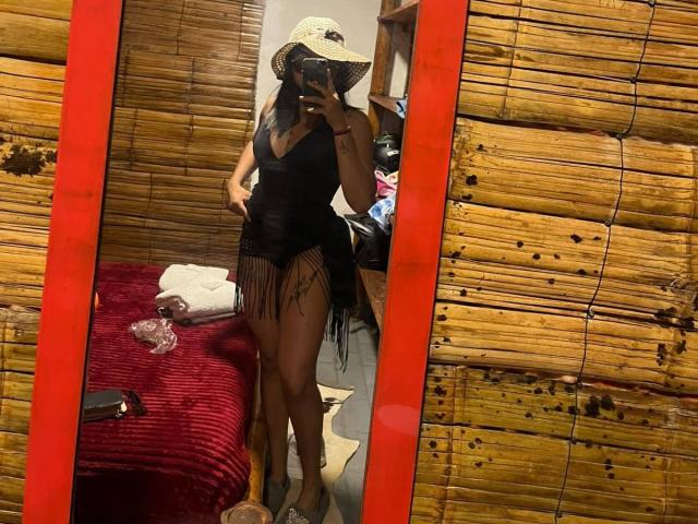 AshlyLee in a black fringed dress, wearing a straw hat, showing off her ass in a mirror, holding her phone, with a red frame and bamboo walls.