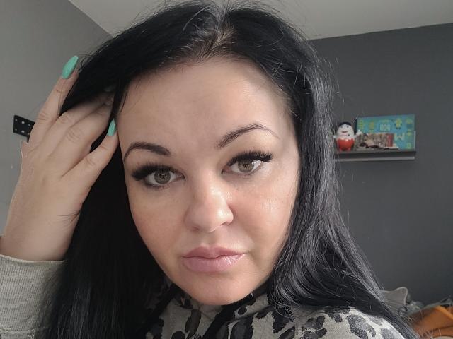 LiaLust has black hair, green eyes, and is pouting with full lips. She's wearing a leopard-print top, touching her hair with turquoise nails. Her tits are small and cute.