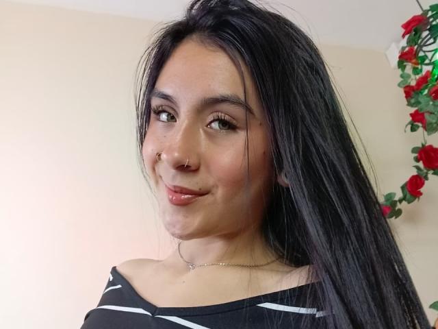 ChloeXk ha lunghi capelli neri, un piercing al naso ed è sorridente con labbra rosa lucide. Indossa una maglietta a righe nere e bianche, che mostra leggermente il seno..