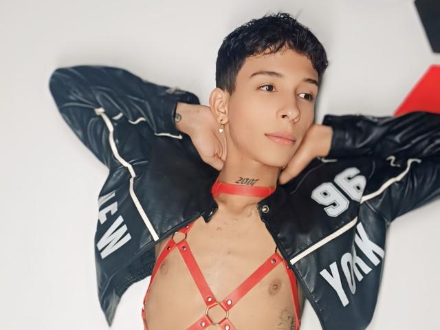 MaxSteeil with short dark hair, wearing a black leather jacket and red harness, exposing his chest with small nipples, hands behind head, tattoo on neck, confident expression.
