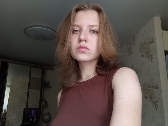VikiCharm ha la pelle chiara, i capelli rossi, gli occhi azzurri e le labbra rosa carnose. Indossa una maglietta marrone senza maniche che mette in mostra il suo seno piccolo. La foto è un selfie..