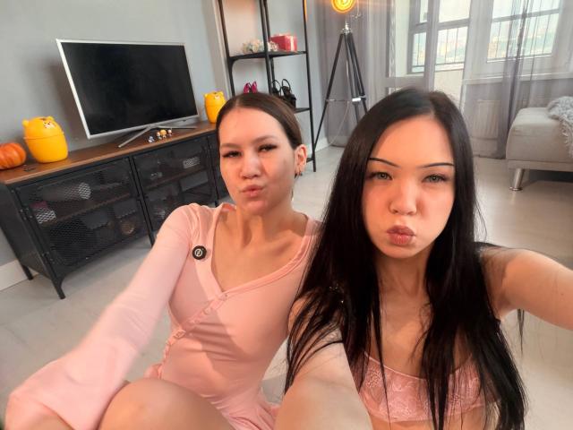 LornaAndGerry, dos mujeres asiáticas con cabello largo y negro, vestidas de rosa, haciendo pucheros a la cámara, sentadas en el suelo, en una habitación moderna con un televisor y calabazas..