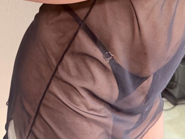 IsadoraVex's sheer black lingerie with a visible black strap and silver ring, showing her butt through the transparent fabric. Her skin is light.
