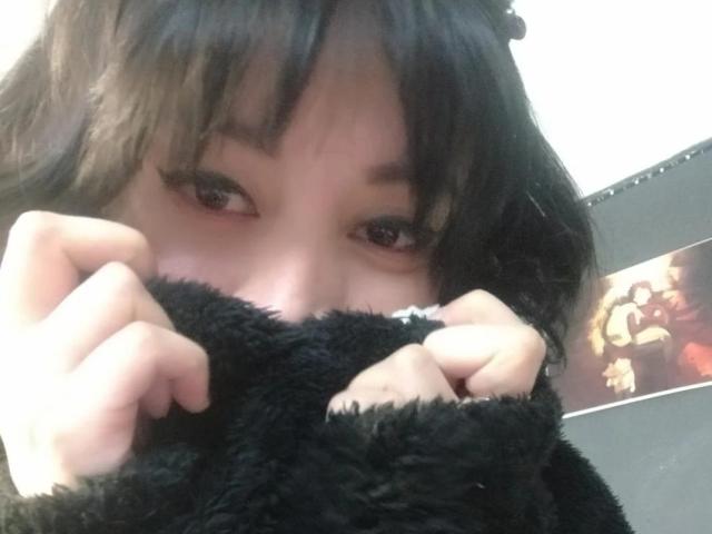 IssisDiosa with black fluffy sleeves covering her face, showing brown eyes and dark bangs, holding the sleeves near her nose, in a slightly blurry selfie.