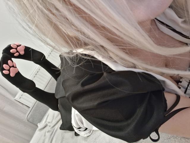 NikaDreamOne's schwarze Socken mit Katzenpfoten-Motiv, rosafarbenen Pfoten-Applikationen, ein schwarzes Kleid und ein weißes Hemd, liegen auf einem Bett, wobei hellblondes Haar einen Teil ihres Gesichts bedeckt..